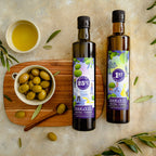 Two bottles of Harvest Extra Virgin Olive Oil and a small bowl of whole green olives on a wooden board, styled with olive branches on a textured beige surface.