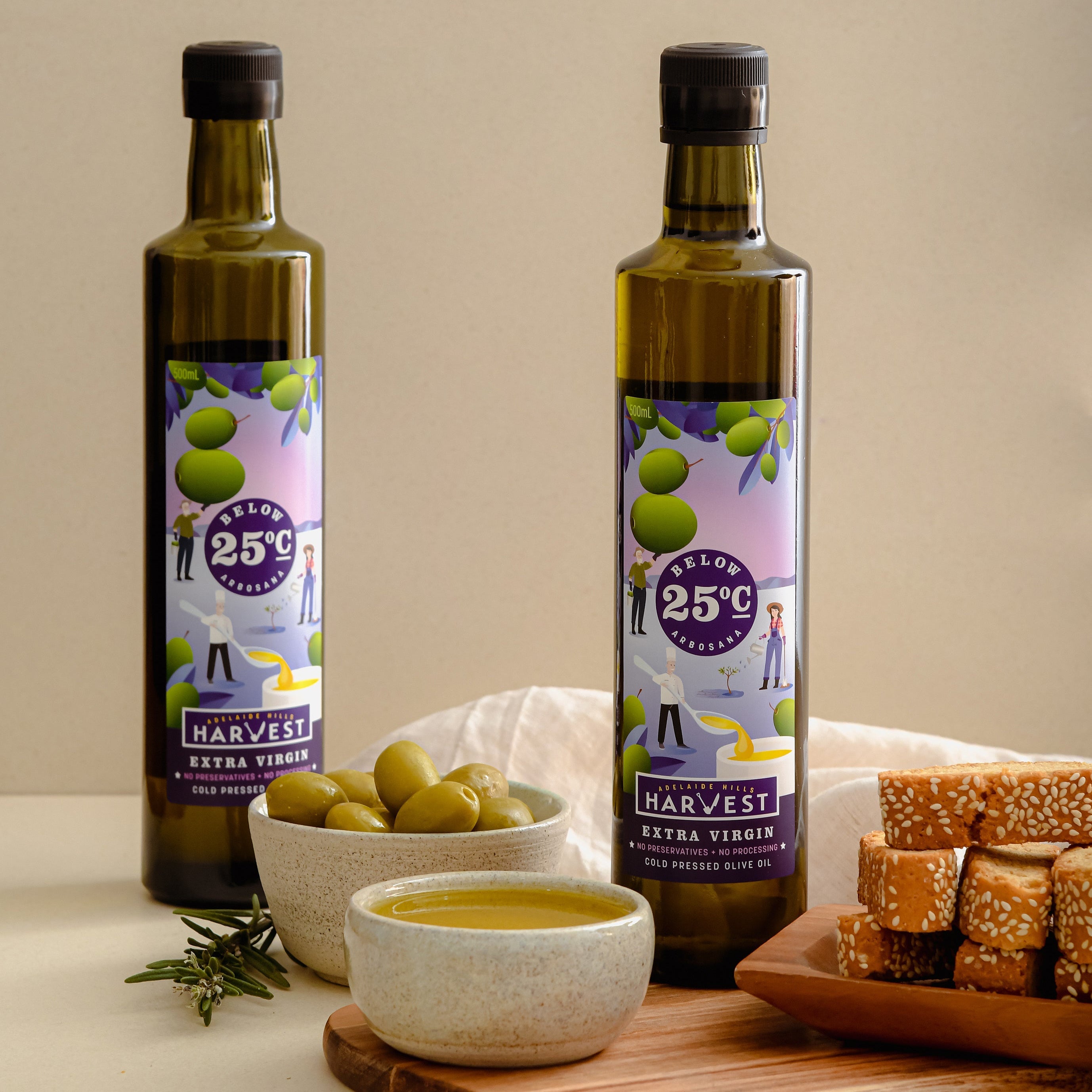 Adelaide Hills Harvest Arbosana extra virgin olive oil bottles with green olives and sesame crackers on a wooden board