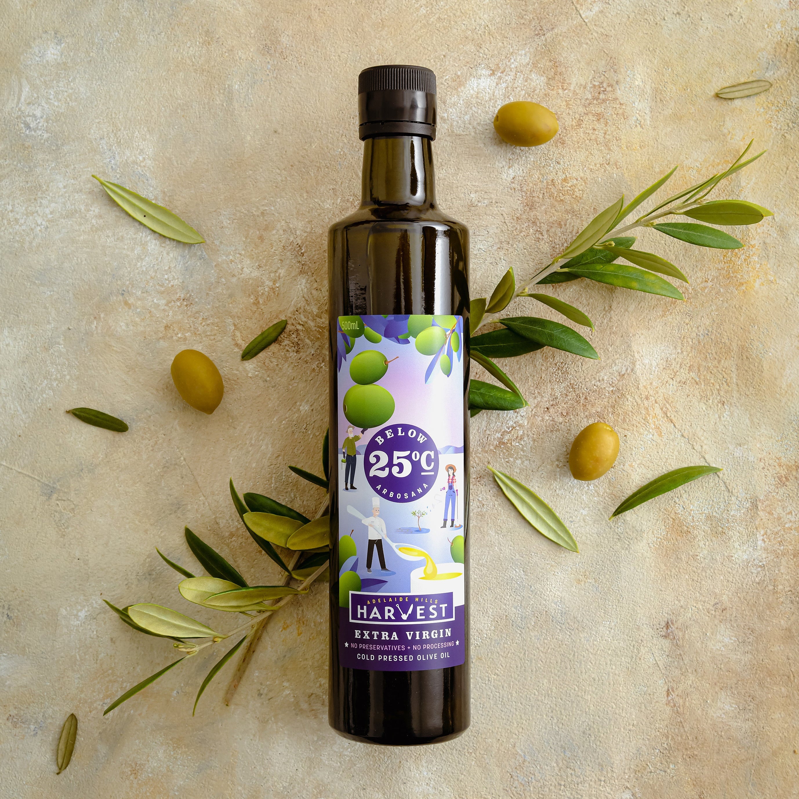 Adelaide Hills Harvest Arbosana extra virgin olive oil in a dark glass bottle surrounded by fresh olives and leaves.