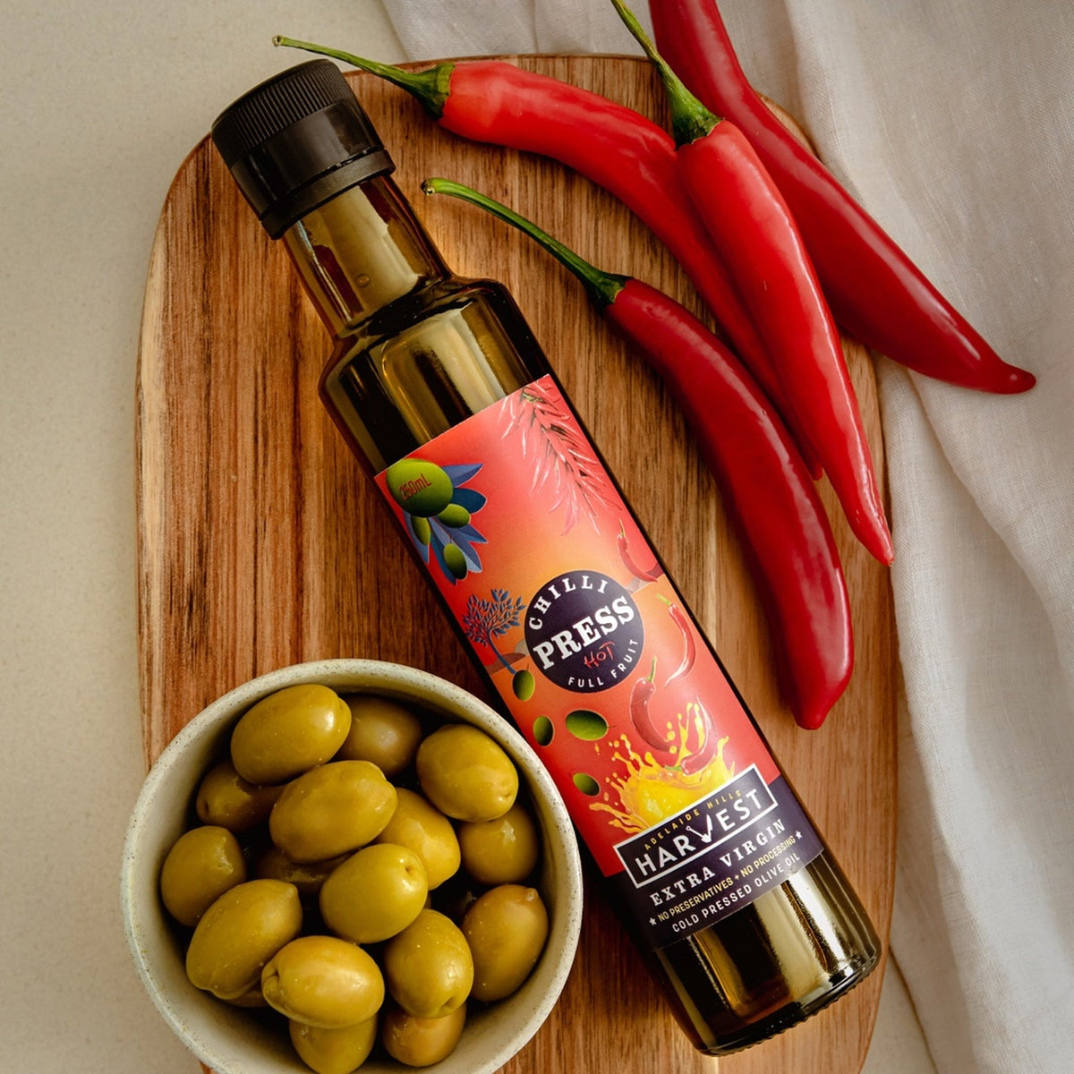 Adelaide Hills Harvest Chilli Press extra virgin olive oil bottle with fresh red cayenne chillies and green olives.