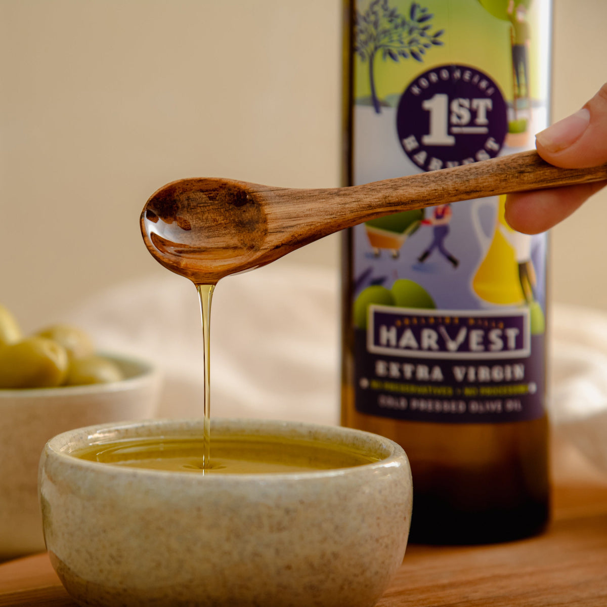 Adelaide Hills Harvest extra virgin olive oil being drizzled from a wooden spoon into a ceramic bowl