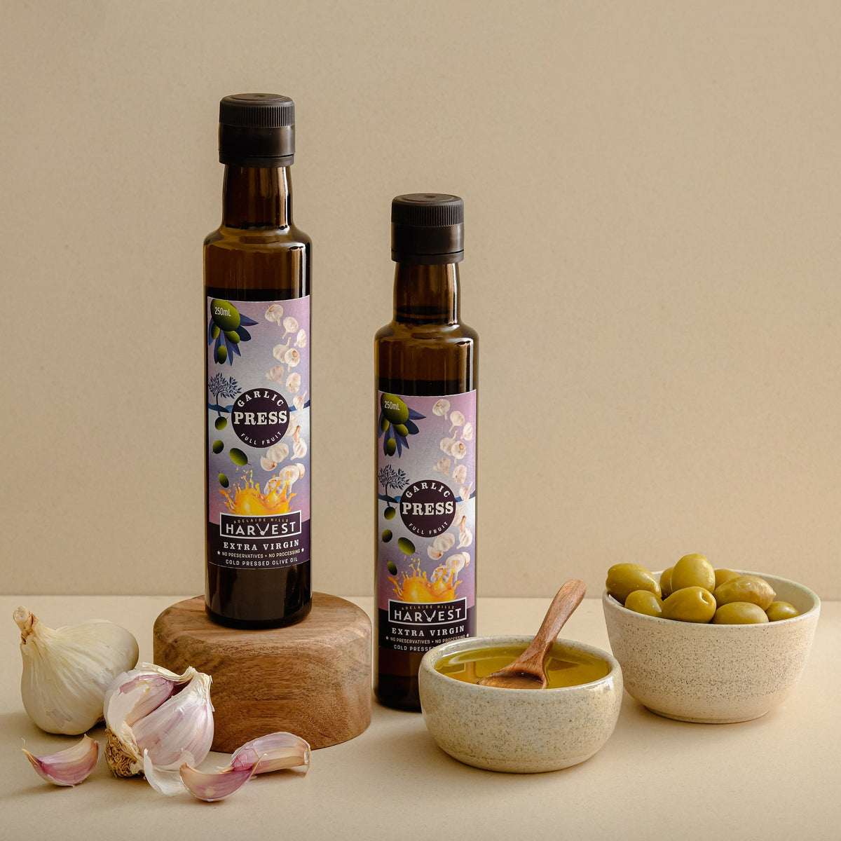 Adelaide Hills Harvest Garlic Press extra virgin olive oil bottles with fresh garlic cloves and a bowl of olives.