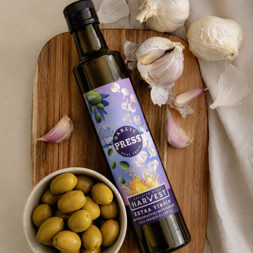 Adelaide Hills Harvest garlic infused extra virgin olive oil bottle with fresh garlic bulbs and green olives on wood