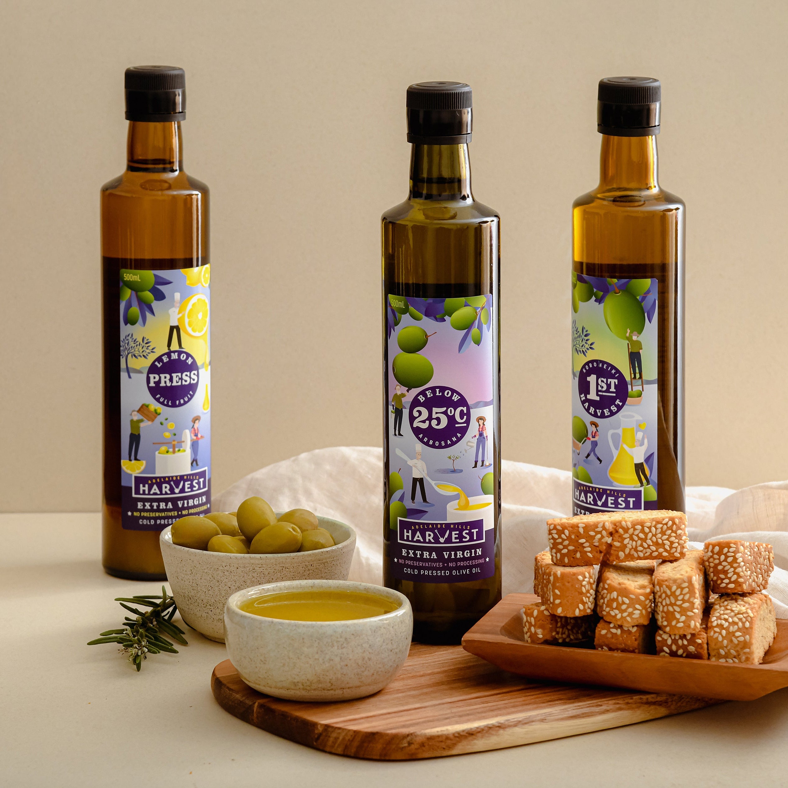 Adelaide Hills Harvest olive oil sample pack with three 500ml bottles, green olives, and sesame crackers on a board.
